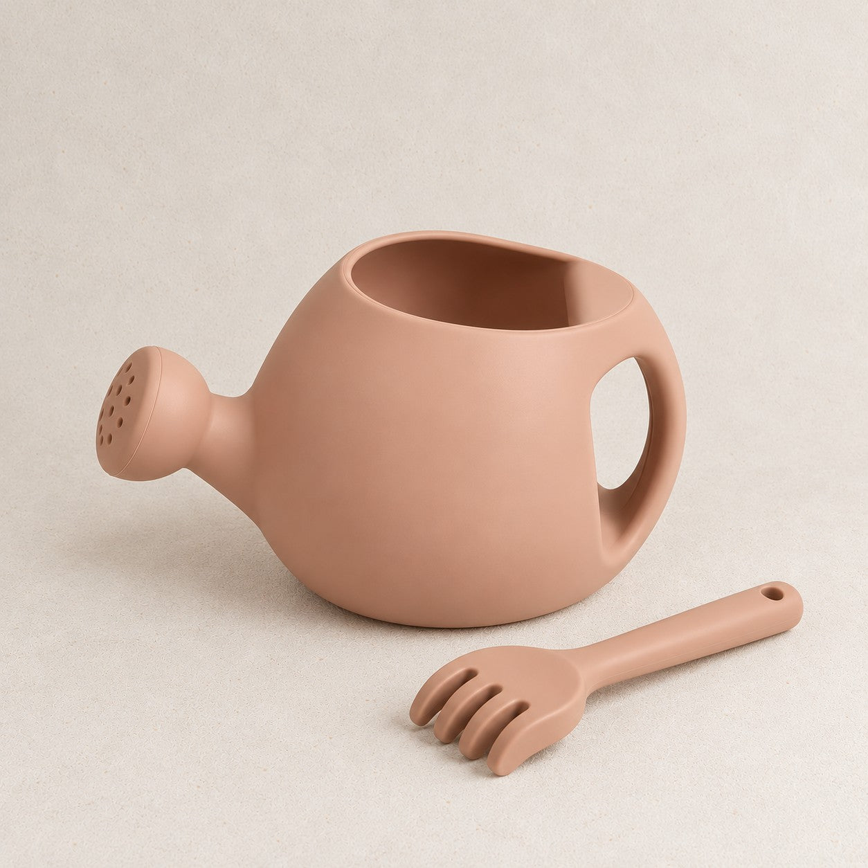 Peach silicone kids watering can and rake set, on a soft stone background