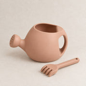 Peach silicone kids watering can and rake set, on a soft stone background