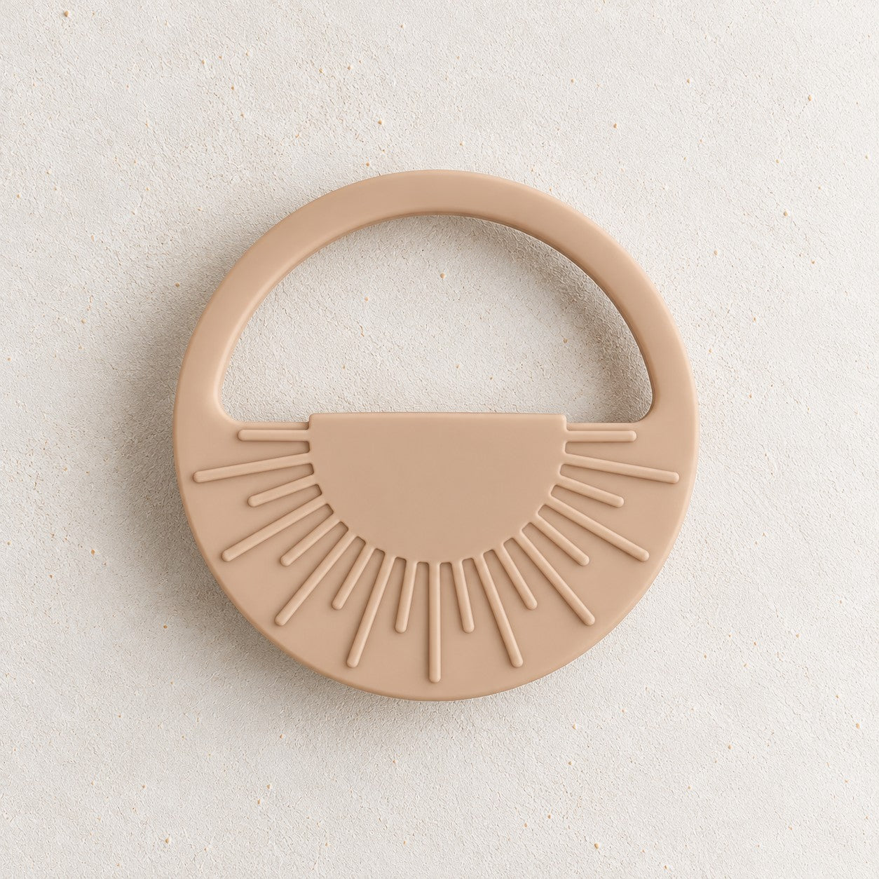 Cream silicone sun teether, a round teether with raised sunrays and an open handle, on a soft stone background