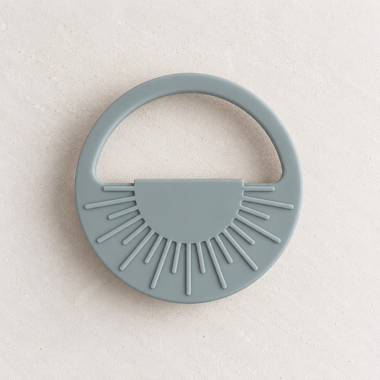 Ether silicone sun teether, a round teether with raised sunrays and an open handle, on a soft stone background